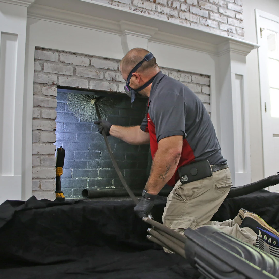 A technician using a chimney brush inside a white brick residential fireplace