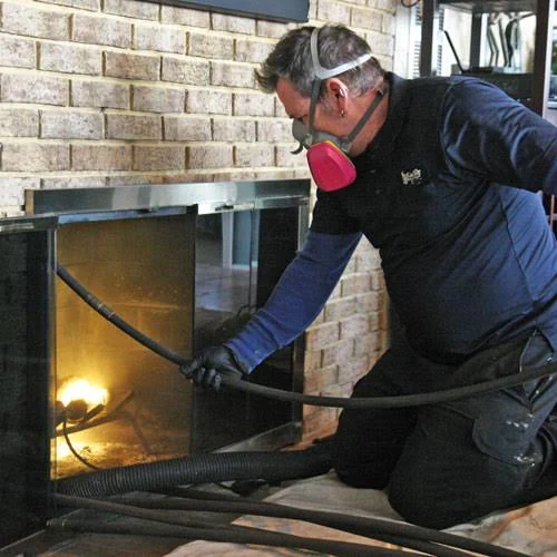A technician wearing a respirator working beside a brick fireplace
