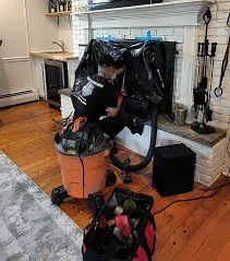 A chimney-service setup with an orange vacuum in front of a white fireplace