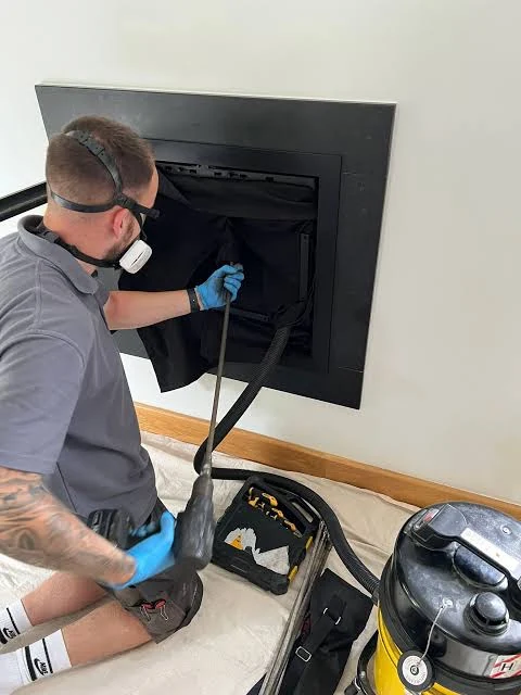 A technician checking an inset fireplace with cleaning tools and a vacuum