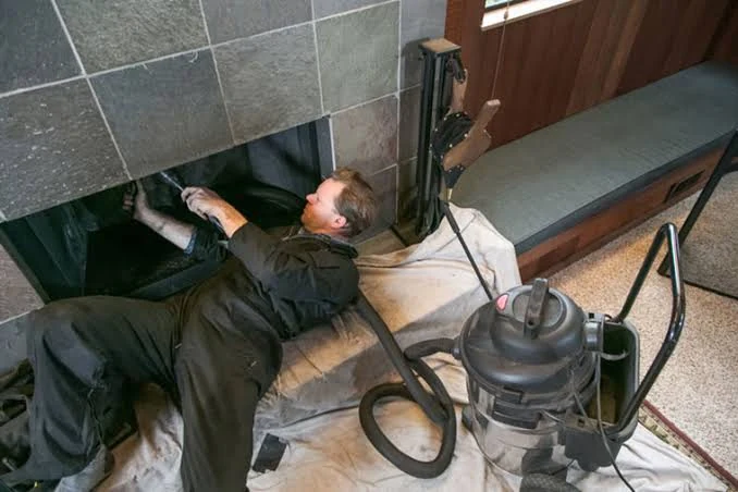 A technician working inside a dark tiled fireplace with a vacuum nearby